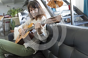 Beauty woman sitting on a dofa and playing guitar