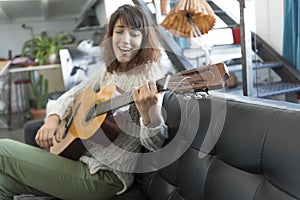 Beauty woman sitting on a dofa and playing guitar