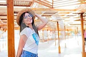 Beauty woman in sunglasses and hat on a pool standing near chaise lounge at summer time