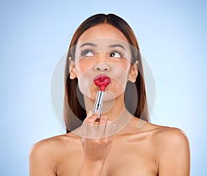 Beauty, woman and thinking about red lipstick or makeup with face cosmetics in studio. Aesthetic female model on a blue
