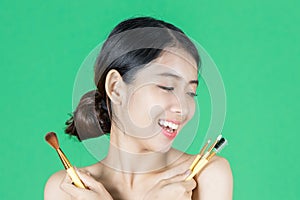 Beauty young Asian woman holding makeup brushes over green isolated background. Healthy and cosmetics concept