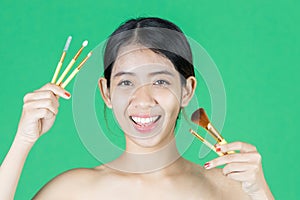 Beauty young Asian woman holding makeup brushes over green isolated background. Healthy and cosmetics concept