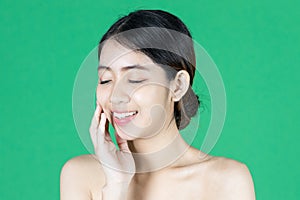 Beauty young Asian woman touching her face over green isolated background. Healthy skin care concept