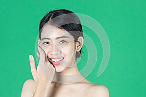 Beauty young Asian woman touching her face over green isolated background. Healthy skin care concept