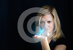 Beauty young blond hair woman holding small glowing blue dinosaur, dragon. Photomanipulation glowing animal on black background