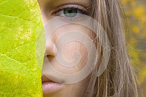 Beauty young blonde woman with green eyes. Teen girl model and green leaf on autumn yellow forest background