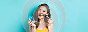 Beauty. Young glamour girl applying make up with pocket mirror and brush, smiling and gazing up at logo, standing