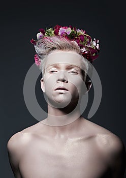 Beauty. Young Man with Wreath of Flowers over Gray