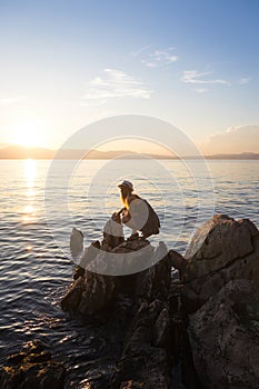 Beauty young woman in dress sitting on rock in sea at sunset. Travel, nature background, Croatia