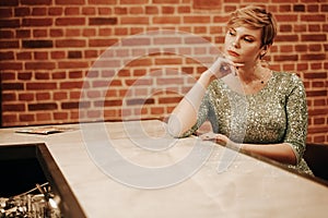 Beauty young woman portrait waiting someone at a bar. Plus size girl in a glitter party dress alone in the cafe.