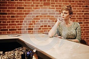 Beauty young woman portrait waiting someone at a bar. Plus size girl in a glitter party dress alone in the cafe.