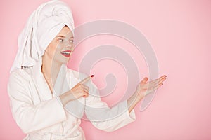 Beauty Young woman with red lips standing in the bath robe and towel on the head on the pink background. Studio shot