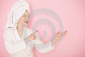 Beauty Young woman with red lips standing in the bath robe and towel on the head on the pink background. Studio shot photo