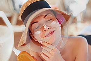 Beauty Young woman with sun cream on face holding sunscreen bottle on the beach