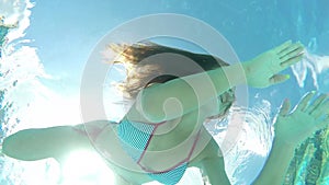 Beauty young woman swimming in bikini underwater in swimming pool waving smiling looking in camera and swim away