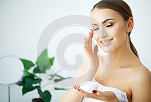 Beauty Youth Skin Care Concept - Close up Beautiful Caucasian Woman Face Portrait applying some cream to her face for skin care.