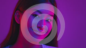 Beauty of youth. Young korean woman smiling to camera, posing in purple neon lights over violet studio background