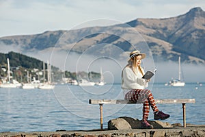 Beautyful asian woman resting is looks at the sea bay with houses and boats on a sunny day at Childrens bay, Akaroa, Canterbury,