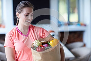 Becoming fit is exercising but more about what you eat. a young attractive woman carrying a bag of groceries at home.