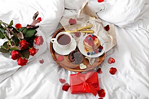 Tray with delicious breakfast, roses and present for Valentine's Day on soft bed