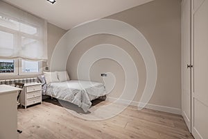 Bed in a bedroom with a whitewood bedside table, wooden flooring