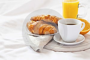 Bed breakfast with coffee cup, croissants and orange juice on wh