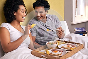 Bed, breakfast and couple with fruit for eating, nutrition and healthy with food in morning. Bedroom, man and woman with