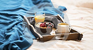 Bed breakfast. Lazy morning breakfast in wooden tray on the bed blanket with muesli and berries bowl, orange juice and coffee