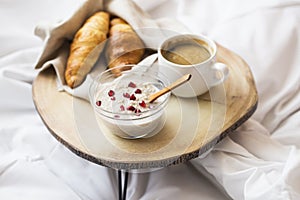 Bed breakfast with porridge bowl, coffee cup and fresh croissants on wooden table on the bed. Selective focus