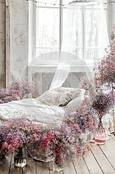 A bed in a bright bedroom in pastel colors in boho style, the trending color of 2023. The room is decorated with lilac and pink