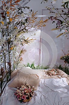 A bed in a bright bedroom surrounded by plants and flowers