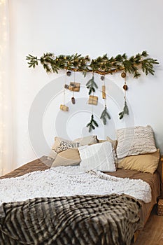 Bed with a Christmas decoration over the head of the bed. Bedroom prepaired for Christmas Eve. New Year decoration