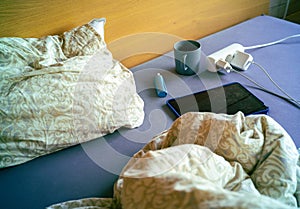 a bed with crumpled bedding, mug and electronic devices, indoor shot