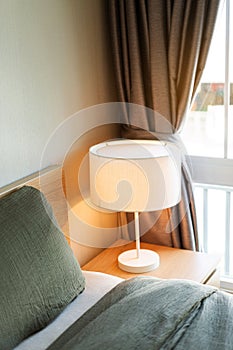 Bed with gray blanket and pillow with white electric lamp on the bedside table in bedroom interior. Minimalist comfort bedroom