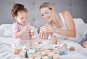Bed, happy mother and baby with toys play together with alphabet education building blocks in home bedroom. Family love
