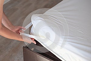 Bed with a high mattress. The woman puts on a protective water-repellent mattress cover