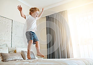 The bed is my trampoline. an adorable little boy jumping on the bed at home.