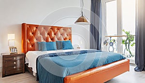 Bed with orange leather headboard and blue bedding. Art deco style interior design of modern bedroom