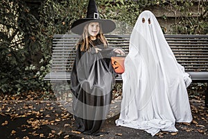 Bed sheet ghost and witch sitting on bench