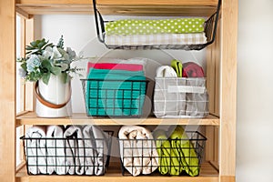 Bed sheets, duvet covers and towels are folded vertically. Metal and fabric black baskets. Bedclothes bright colors