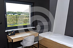 A bed and a table in a modern boy room in black and white colors, with vinyl panels on the floor.