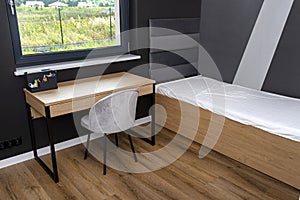 A bed and a table in a modern boy room in black and white colors, with vinyl panels on the floor.