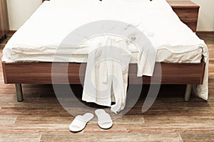 Bed with white linens and white bathrobe with slippers in hotel