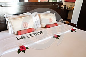 bed with white pillows and a coverlet, decorated with tropical flowers and an inscription - welcome. Theme of hotel service