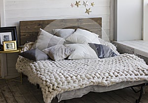 Bed with wooden headboard, pillows, knitted blanket. Scandinavia