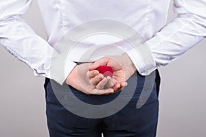 Bedind rear view photo of excited nervous gentleman hiding small bright red box with ring behind back isolated grey background