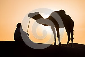 Bedouin and camel on way through sandy desert Beautiful sunset with caravan on Sahara, Morocco Desert with camel and nomads