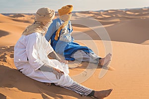 Bedouin nomad, Sahara desert, Morocco. Portrait of a Bedouin nomad with colorful turban and big smile sitting on sand dune.