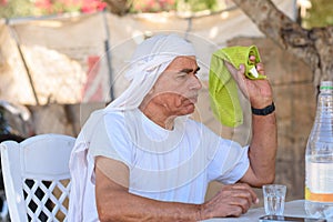 Bedouin senior tries to swat fly with towel. Old Arabic man in traditional clothes outdoor portrait.