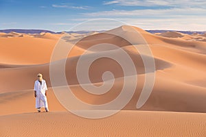 Bedouin on way through sandy desert. Beautiful sunset with big dunes on Sahara, Morocco. Silhouette nomad man.